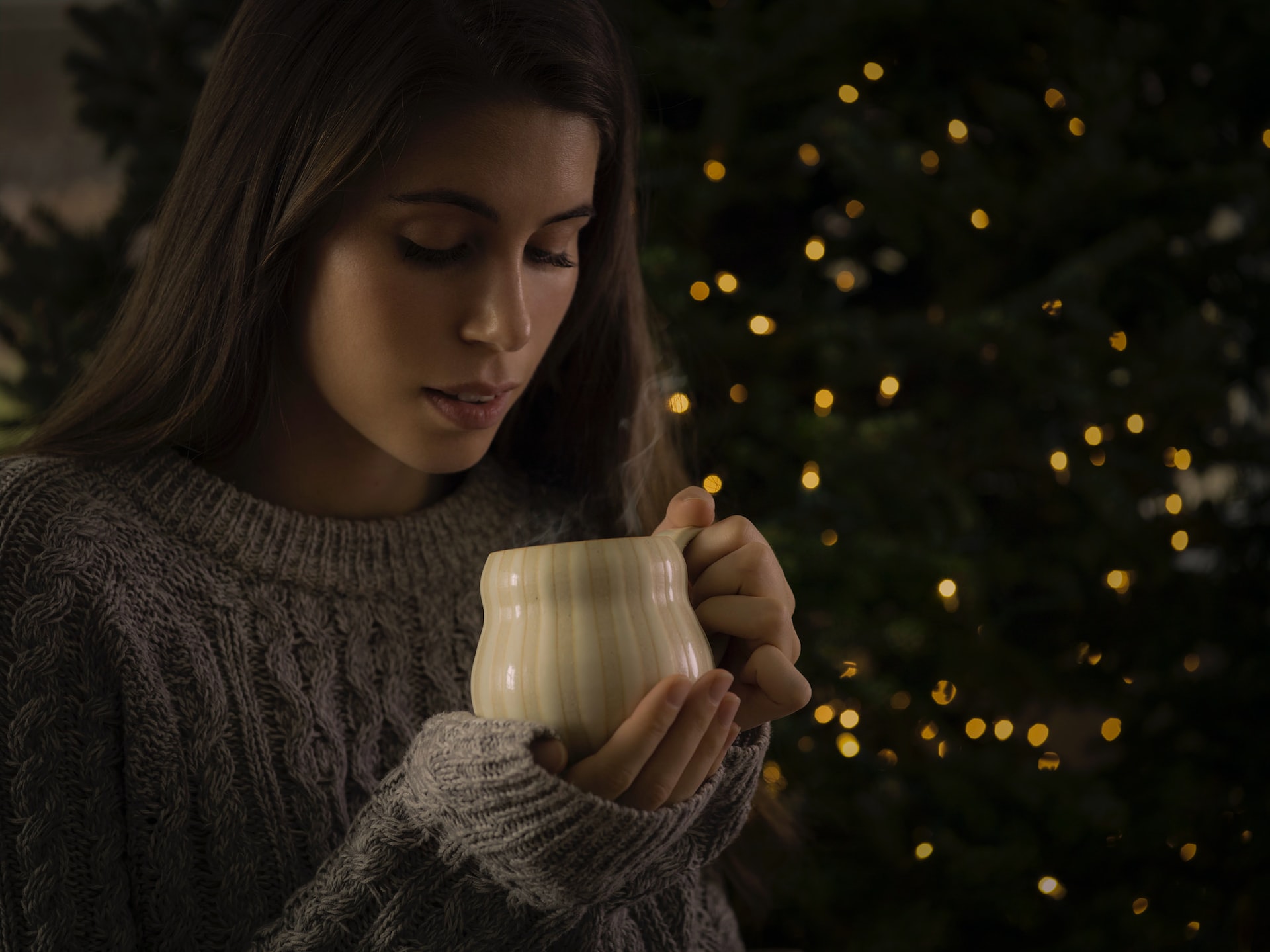 man holding white ceramic mug standing in front of lighted green Christmas tree